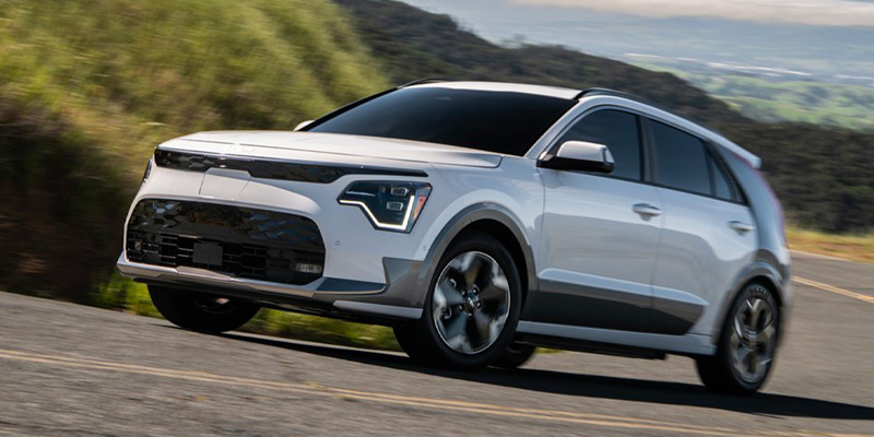 White 2025 Kia Niro-EV driving down mountain road.